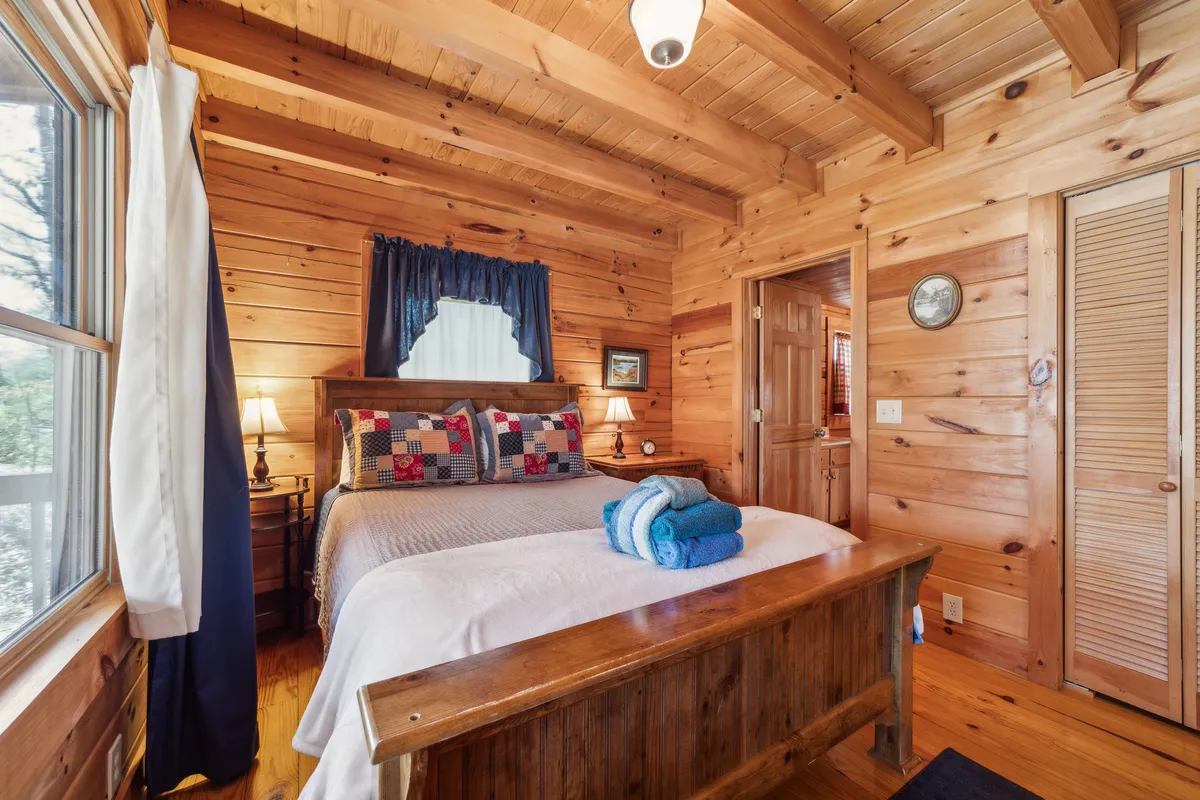 A cozy bedroom featuring a comfortable bed dressed with decorative pillows, warm lighting from bedside lamps, and neatly folded towels. The atmosphere is relaxing, making it ideal for restful nights or quiet reading by the window.