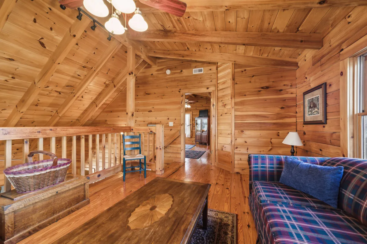 A welcoming lounging area featuring wooden beams, a plaid sofa, coffee table, blue chair, and a basket. The space feels open, comfortable, and perfect for group gatherings, reading, or enjoying a cup of coffee by the window.