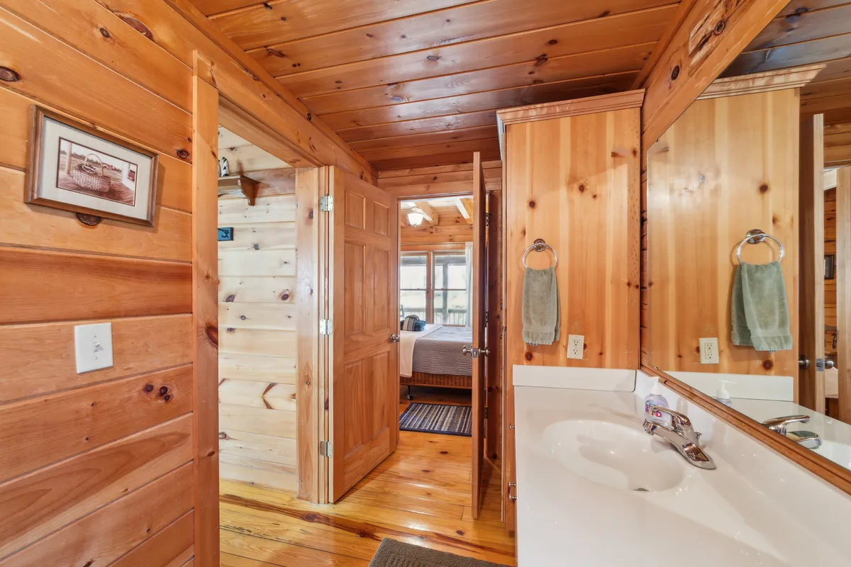 A warmly lit space with rustic wooden paneling, a mirror above the sink, and open doorways, creating an intimate and inviting interior. The soft lighting and comforting textures evoke a sense of home and relaxation, ideal for unwinding after a day of outdoor exploration.