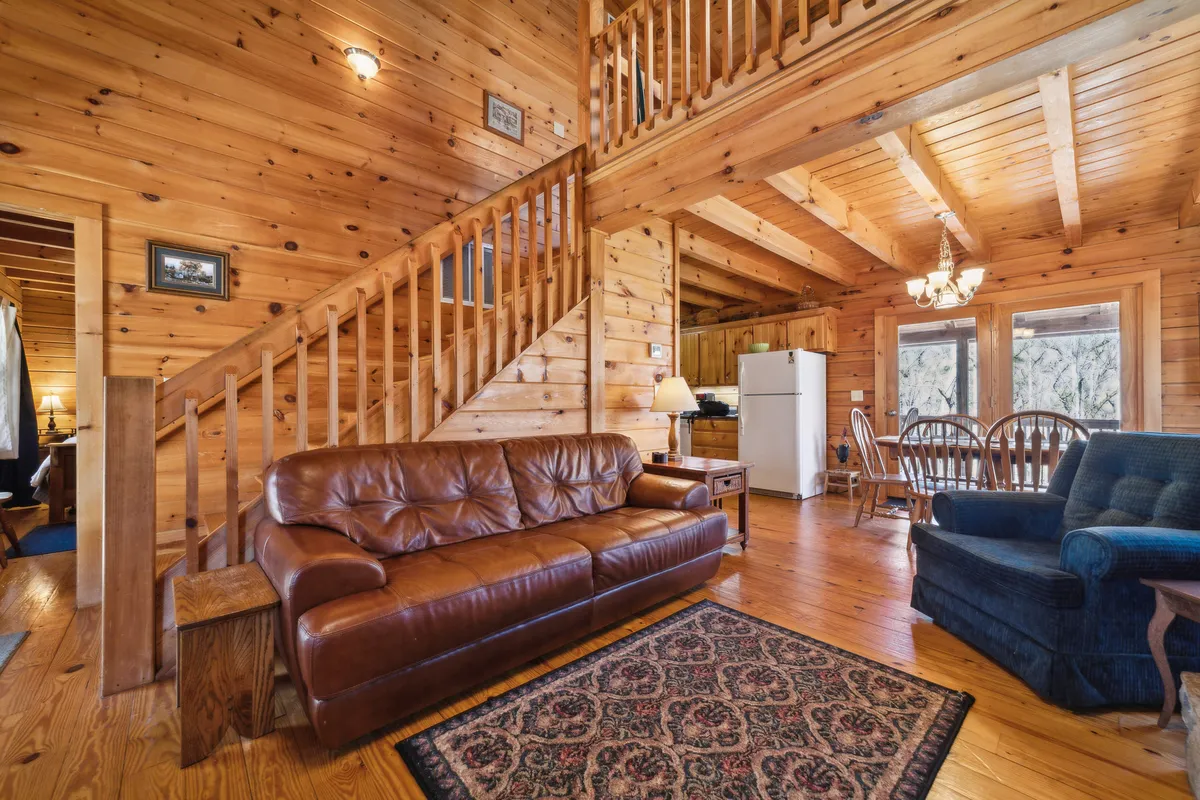 This interior shot showcases a spacious living area featuring a leather sofa, wooden staircase, dining table, and large windows. The arrangement invites communal activities—family gatherings, holiday celebrations, and game nights—while the open layout reflects the flexible accommodations described in the section.