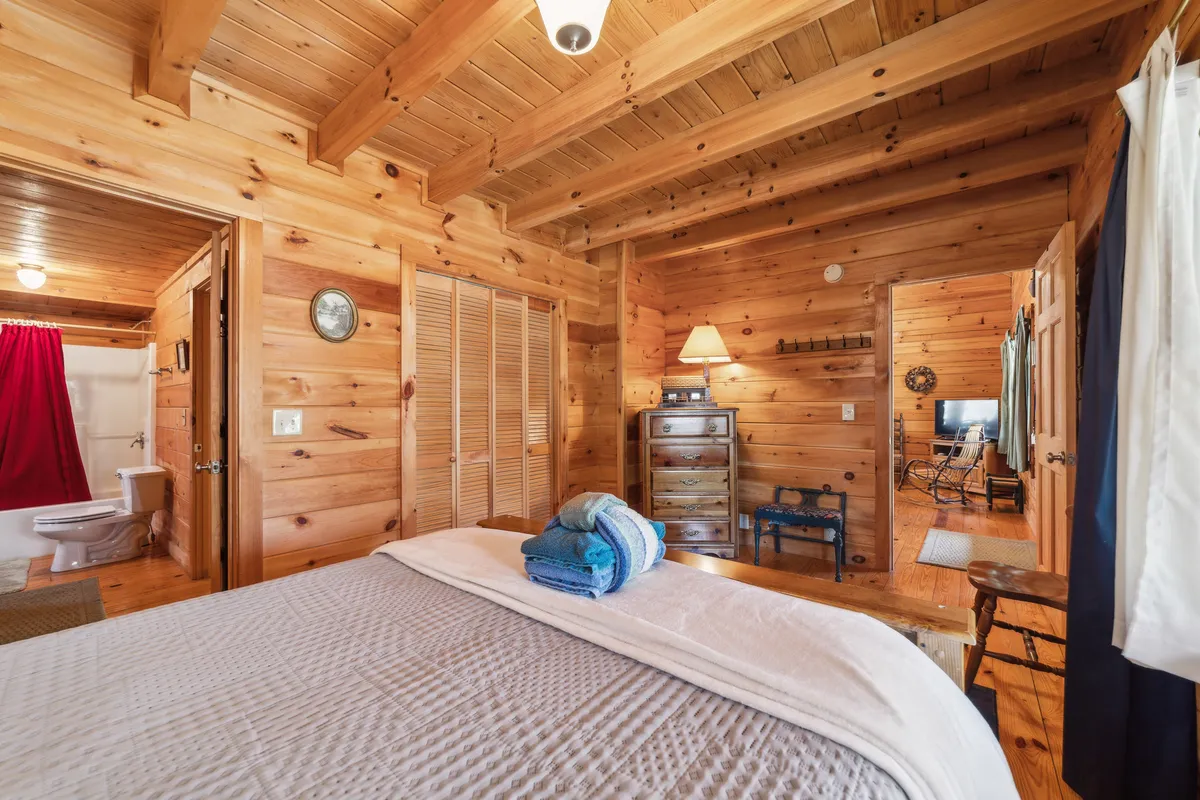 A snug nook with wooden ceiling beams, a bed with neatly arranged towels, a vintage dresser, and a soft lamp glow. The warm, intimate setting invites moments of quiet relaxation, reading, or unwinding alone or with family.