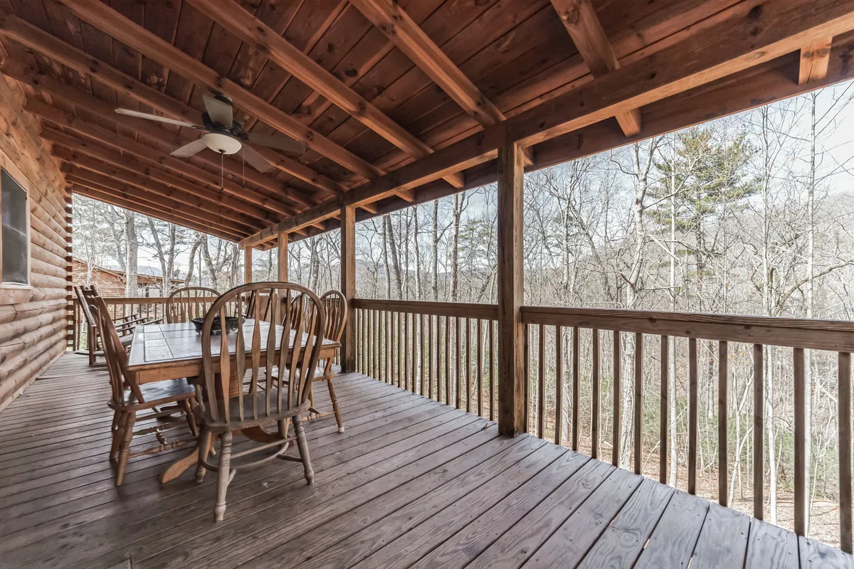 An inviting outdoor dining area with a wooden table and chairs sits beneath a ceiling fan, overlooking a beautiful natural landscape. The setting feels open, fresh, and perfect for communal experiences in the outdoors.