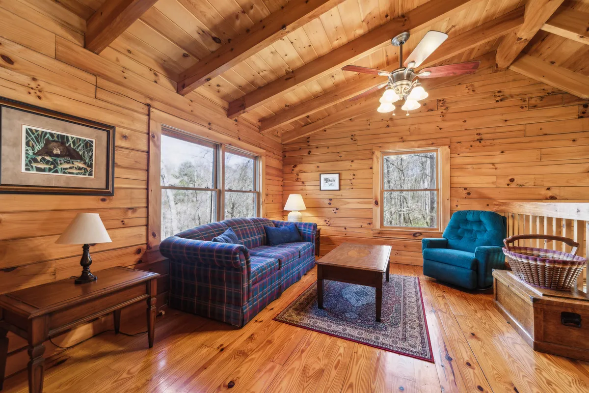 A cozy corner with a plaid sofa, wooden coffee table, blue armchair, and warm lighting, perfect for relaxing, playing games, or enjoying quiet bonding moments. Art on the wall and the inviting setup suggest a space designed for group activities and socializing.